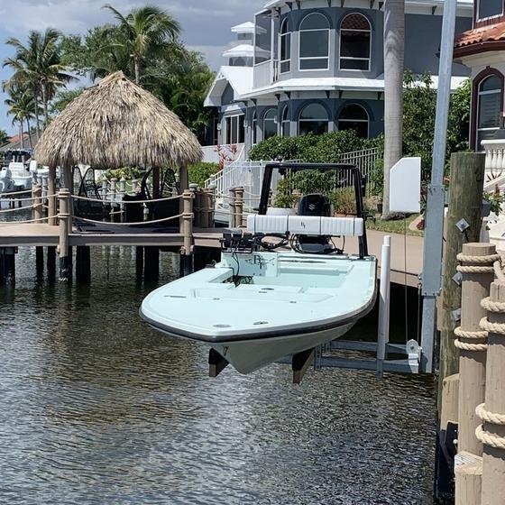 Flats skiff raised on a piling lift in front of a tiki hut