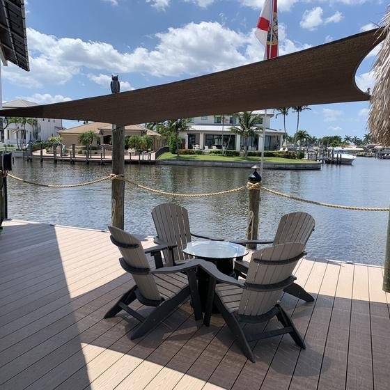 Adirondack chairs on a Brownstone vinyl dock under a shade sail next to a tiki hut